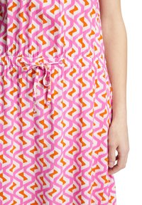 Robe rose présentant un motif géométrique en zigzag blanc et orange, avec une taille élastique et un lien ajustable. Tissu doux et léger.