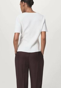 Top bianco a maniche corte con una leggera lucentezza, dotato di scollatura rotonda e vestibilità morbida, abbinato a pantaloni a gamba larga marrone scuro.