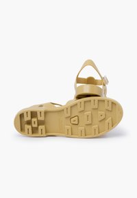 Yellow rubber sandal with adjustable ankle strap, textured sole for grip, and a contoured footbed. Drainage holes are visible on the bottom.