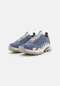 Niebieskie sneakersy na zewnątrz z teksturowaną cholewką, wzmocnionym czubkiem, szarymi sznurowadłami oraz gumową podeszwą z wyraźnymi bieżnikami zapewniającymi przyczepność.