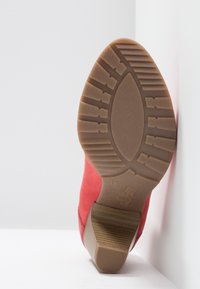 Semelle d'une botte rouge à talon avec une bande de roulement en caoutchouc texturée et un talon empilé de hauteur moyenne sur fond blanc.