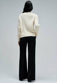 Crème ribbeltrui met verlaagde schouders, gecombineerd met zwarte wijde broek; achterkantaanzicht dat textuur en pasvorm toont.