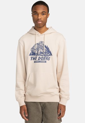 Krämfärgad hoodie med en blå grafisk design och texten "THE DOERS" samt skogsdetaljer. Framtida känguruficka och ribbade ärmslut.