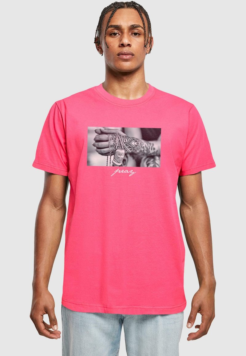 Rožinė medvilninė marškinė, su juodai balta nuotrauka centre, vaizduojančia tatuiruotą ranką, laikantį grandines, o po ja – balti žodžiai „melskis“.