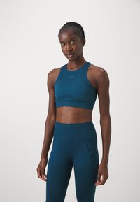 Sujeción deportiva en color teal y leggings de tiro alto hechos de un material texturizado, con costuras ergonómicas y un logo en la zona del pecho.