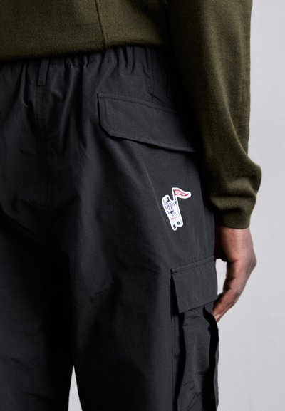 Svart cargobukser med elastisk midje, sidelommer og en brodert astronautdesign med et flagg på høyre lomme.