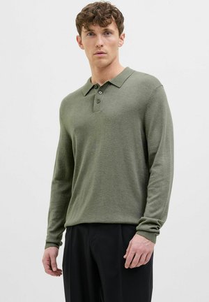 Long-sleeve green polo shirt made from soft fabric, featuring a collar, three buttons, and ribbed cuffs. Paired with black trousers.