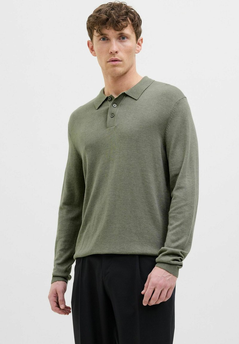 Garās piedurknes zaļš polo krekls, izgatavots no mīkstas auduma, ar apkakli, trim pogām un ribotām piedurknēm. Saskars ar melnām biksēm.