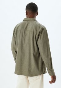 Olivgrünes Button-Up-Hemd aus strukturiertem Stoff, mit Rückenpasse, langen Ärmeln und lässiger Passform.