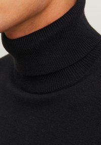 Svart polotröja i mjukt stickat tyg med ribbad struktur. Har en hög, åtsittande krage och en slät kroppdesign.