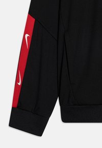 Mustaga spordi jakk punaste külgpaneelidega. Omab valget Nike logo varruka peal. Valmistatud siledast kangast ja ribakujuliste varrukateotstega.