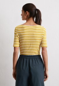 Geel en wit gestreepte korte mouwen top, ronde halslijn, gecombineerd met donkere broeken met een elastische tailleband en een achterzak.
