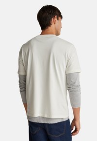 Bílý tričko s krátkým rukávem položené na šedém tričku s dlouhým rukávem. Neformální design s volným střihem a hladkou texturou.