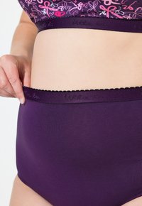 Mutande alte di colore viola con una texture liscia e una cintura elastica. La cintura presenta bordi ondulati e un marchio impresso.