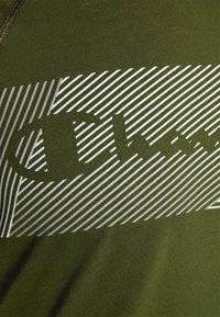 Tejido verde con un diseño rectangular de rayas diagonales en blanco y gris, superpuesto a texto en negrita parcialmente visible.