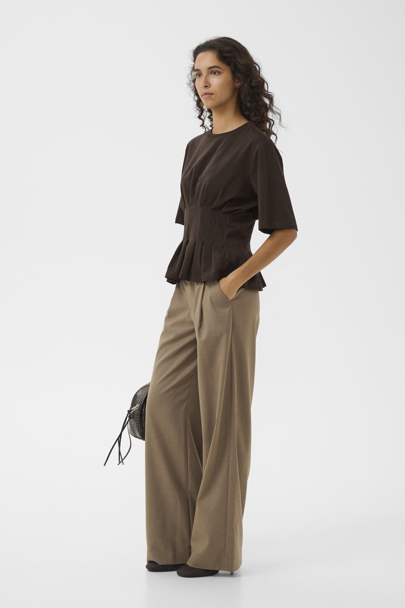 Haut peplum marron à manches courtes, associé à un pantalon large beige. La tenue présente une texture lisse et une silhouette classique, complétée par un sac tissé.