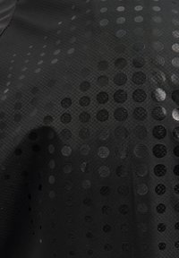 Svart textil med ett subtilt mönster av prickar i olika storlekar som är delvis reflekterande, ordnade i en gradient, med en jämn, matt yta.