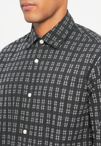 Man in een zwart-wit gestreepte button-up shirt met een puntige kraag, weergegeven van de nek tot halverwege de borst.