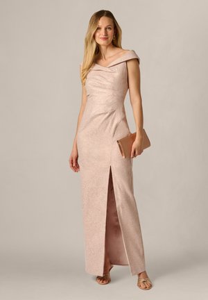 Kvinde i en lyserød skulderløs aftenkjole med frontslids, der holder en rose gold clutch og bærer guld sandaler og øreringe.