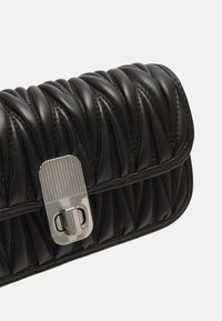 Czarna skórzana kopertówka o pikowanej fakturze, z prostokątnym zapięciem w kolorze srebrnym i subtelnymi detalami w postaci stężeń. Kompaktowy i owalny kształt.