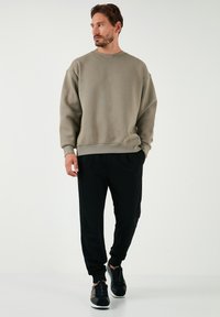 Sudadera gris claro con cuello redondo, mangas anchas y dobladillo acanalado, combinada con pantalones de chándal negros ajustados y zapatillas negras.