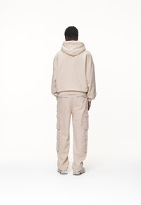 Beige bomullshuvtröja med oversized passform och ribbade cuffar, tillsammans med matchande beige cargobyxor med flera fickor och raka ben.