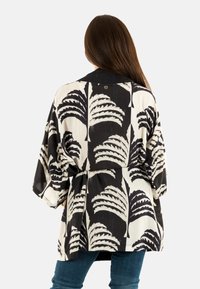 Kimono en blanco y negro con un patrón de hojas, corte holgado, mangas anchas y un cinturón. Fabricado en tela ligera con una textura suave.