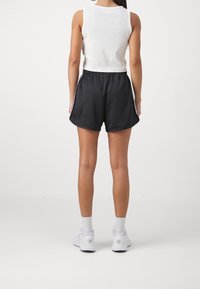 Černé sportovní šortky s bílými bočními pruhy, spárované s přiléhavým bílým tílkem. Lehká tkanina a sportovní design, zobrazené zezadu.