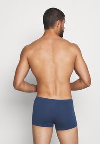 Boxers en coton bleu avec une coupe ajustée, présentant une texture lisse et un taille mi-haute. Coutures visibles autour des bords.