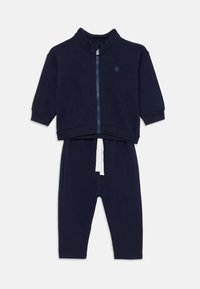 Mörkblå träningsoverall med zip-up jacka och långa byxor. Mjukt tyg, hög krage och vit dragsko på byxorna. Enkel, enfärgad design.