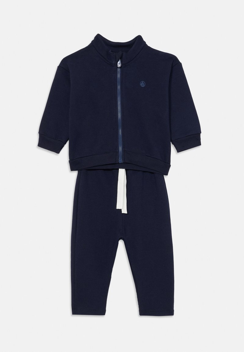 Mörkblå träningsoverall med zip-up jacka och långa byxor. Mjukt tyg, hög krage och vit dragsko på byxorna. Enkel, enfärgad design.