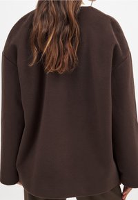 Suéter de forro polar marrón con un ajuste relajado, hombros caídos y escote redondeado. Textura suave, diseño minimalista, sin cierres visibles.