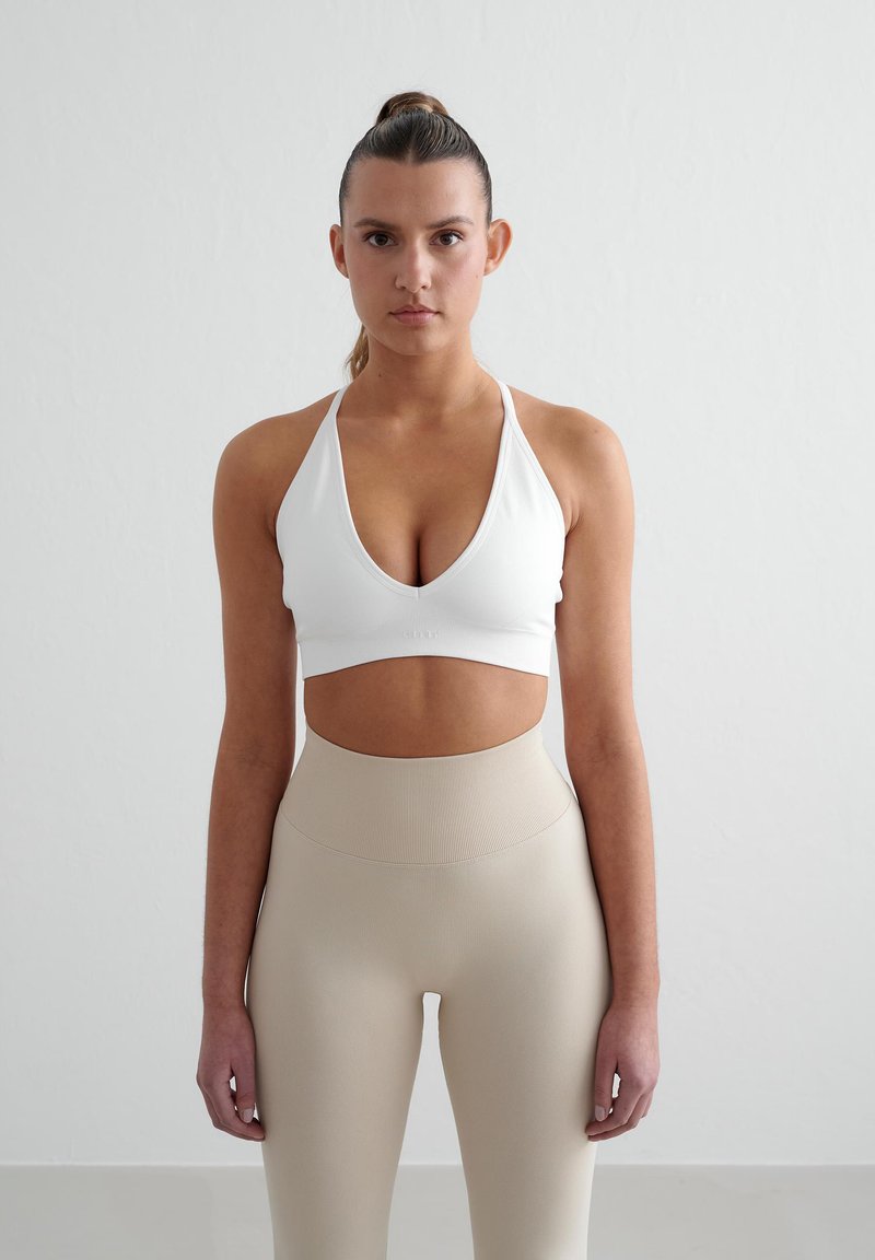 Witte sportbeha met een diepe V-hals, gecombineerd met beige high-waisted leggings met een gestructureerde afwerking.