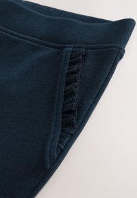 Tessuto blu navy con dettaglio arricciato sulla tasca laterale, texture liscia e cintura morbida ed elastica.