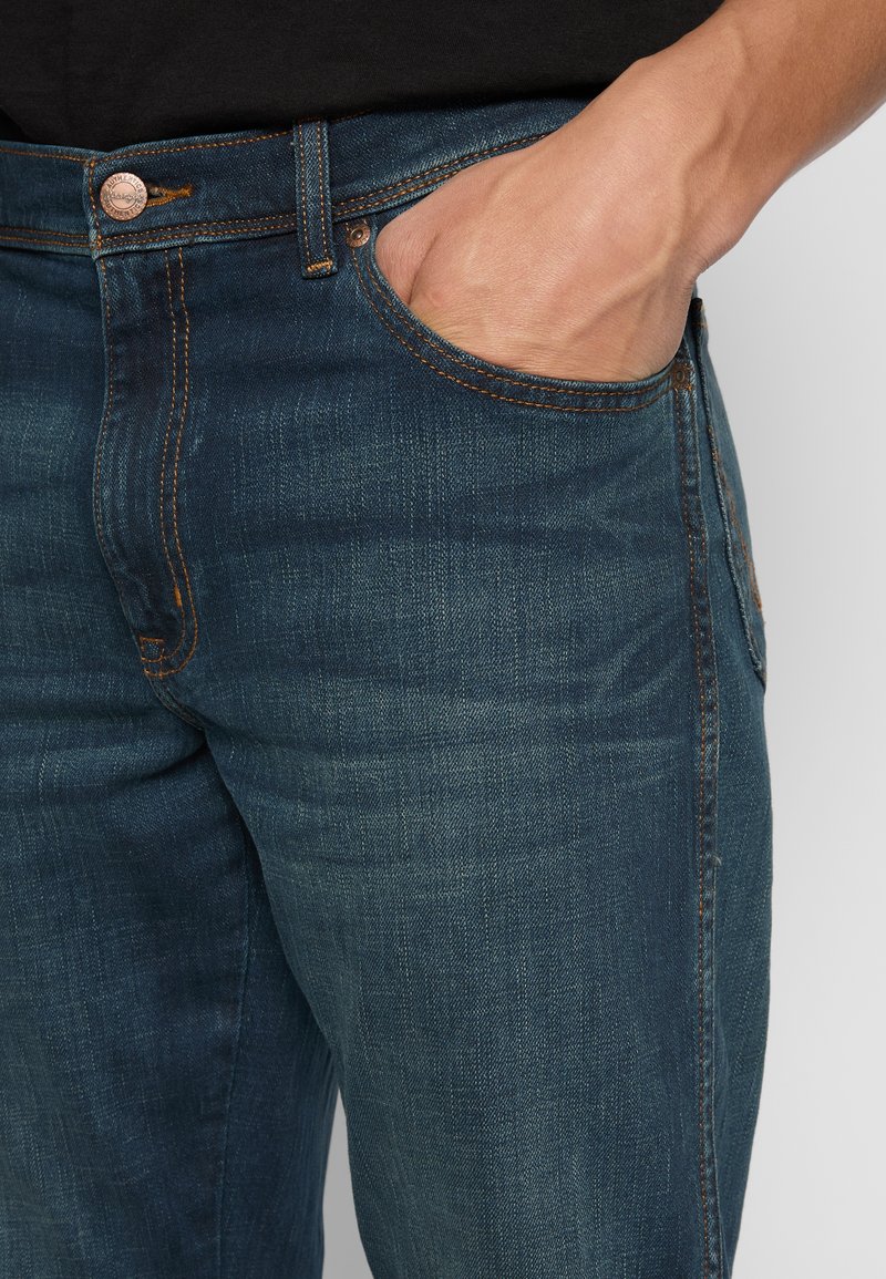 Niebieskie dżinsy o slim fit, z miedzianymi elementami, pomarańczowymi szwami, przednimi kieszeniami i delikatnym efektem wyblaknięcia.