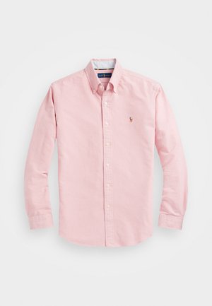 Chemise rose pâle à manches longues avec boutons, col et petit logo brodé sur la poitrine gauche sur fond uni.
