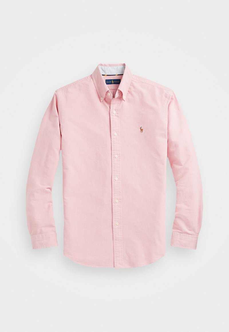 Chemise rose pâle à manches longues avec boutons, col et petit logo brodé sur la poitrine gauche sur fond uni.