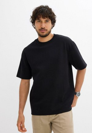 T-shirt in cotone nero con collo rotondo e maniche corte, caratterizzato da una vestibilità comoda. Indossato con pantaloni khaki e un orologio in argento.