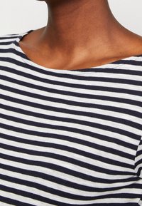 Bluzka w paski w kolorze granatowym i białym, poziome paski, miękka tkanina oraz dekolt w łódkę. Subtelna tekstura i luźny krój.