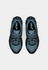 Idrottsskor med en mesh-övre i teal och svart, med texturerade detaljer, dämpad sula och traditionell snörning.