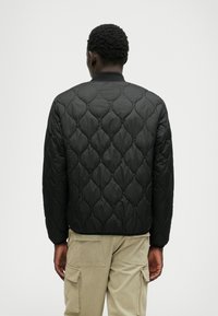 Schwarze gesteppten Bomberjacke mit einem strukturierten Muster, elastischen Bündchen und Kragen. Wird mit khakifarbenen Cargo-Hosen getragen.