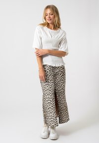 Top bianco con smock e maniche corte abbinato a una gonna maxi con stampa leopardata e spacco laterale, indossato con sneakers bianche chunky.