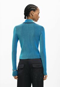 Niebieski prążkowany sweter z długimi rękawami i wysokim kołnierzem, z gradientowym wzorem przechodzącym od jasnego do ciemnego niebieskiego.