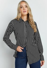 Camicia a maniche lunghe a righe bianche e nere con chiusura a bottoni, dotata di due tasche sul petto e colletto a punta, realizzata in un tessuto morbido.