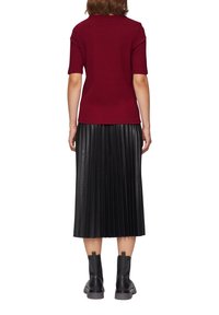 Top corto de manga corta rojo acanalado, combinado con una falda midi de piel negra con pliegues. Botines negros completan el atuendo.