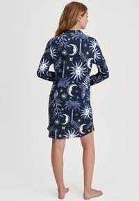 Camicetta da notte blu navy con un motivo celestiale che presenta disegni di sole, luna e stelle. Realizzata in tessuto morbido, con maniche lunghe e spacchi laterali.