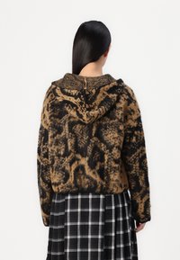 Sudadera con estampado de leopardo marrón y negro, con un tejido texturizado y capucha, combinada con una falda de cuadros en blanco y negro.