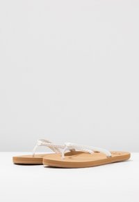 Valkoiset flip-flop-sandaalit, joissa on punotut hihnat, vaaleat kumipohjat ja sileä pinta. Hihnoissa on letitetty muotoilu lisäyksinä.