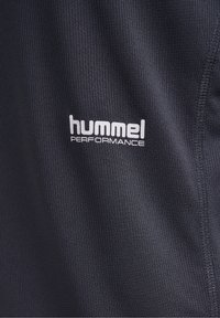 Tissu texturé foncé avec le logo blanc « hummel PERFORMANCE » imprimé près de la couture cousue sur le côté droit.