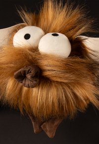 Plush toy head with exaggerated features: large white eyes, spiky orange-brown fur, and a dark brown fabric nose with a scrunch detail.